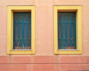 Two windows with green shutters on orange walls.