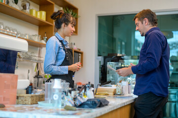 Young service minded barista woman with customer in coffee shop