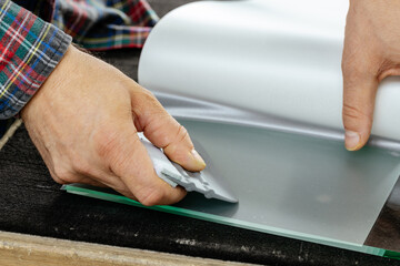 A specialist glues a special protective and decorative foil to the glass with a special tool