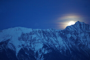 full moon rising over the  snowy mountains in the southern alps france