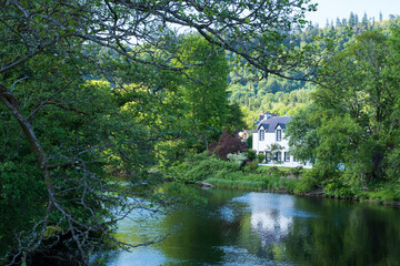 Fototapeta premium Loch view with white painted house on the far shore, in remote area in thee highlands of Scotland, UK. House is reflected in the water.