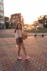 beautiful little girl in the city at sunset. A girl in a white blouse and with a straw hat is having fun outside