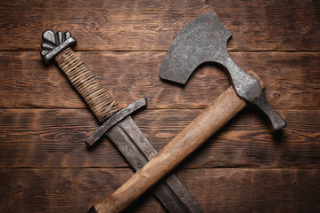 Old battle sword and axe on the wooden table background.