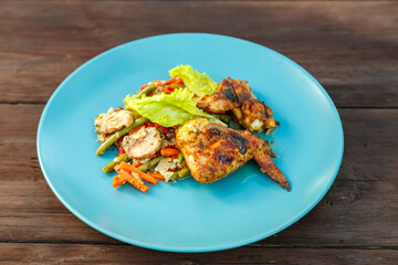 Blue plate with chicken and vegetables on a wooden table. horizontal photo