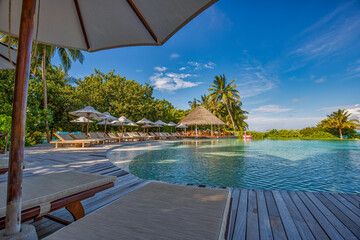 Outdoor tourism landscape. Luxurious beach resort with swimming pool and beach chairs or loungers under umbrellas with palm trees and blue sky. Summer travel and vacation background concept

