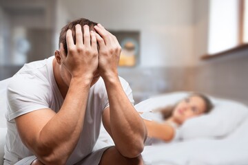 Upset young man in pajamas waking up with headache, lying in bed early in morning, touching his...