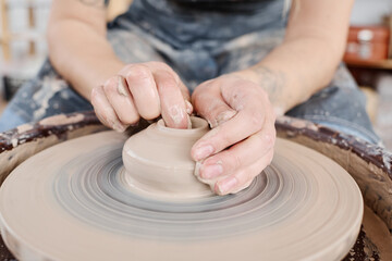 Hands of young female potter on raw clay item on rotating pottery wheel during creation of new earthenware for sale in handcraft shop