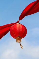 Obraz premium Red Chinese lantern in the air decorating the streets of China. Traditional Asian decor for new year celebrations in beautiful sky background. Creative cultural art hanging high up on a summer day