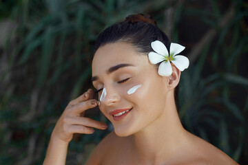 Beauty Woman Concept. Skin care. Young model with Soft skin holding cosmetic cream. Portrait of female applying moisturizing cream and touch own face in tropical nature