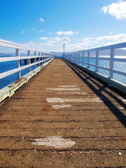 Fototapeta premium A wood pier leading into the ocean with copy space. An old empty platform or dock terrace on a lake with blue water. Wooden jetty, old bridge or a wharf near a lakehouse getaway retreat during summer