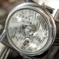 Closeup of a round headlight on a classic motorbike. One light bulb on a well maintained sliver chrome coated retro motorcycle. Motor vehicle accessories and parts. Glass lamp light with silver fram