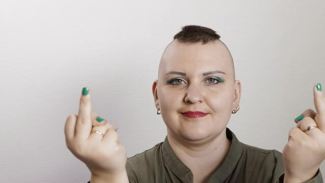 A shaved woman with a mohawk smiles showing a fuck to the camera.
