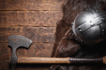 Viking axe, helmet and beast skin on the wooden table flat lay background with copy space.