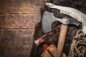 Fototapeta Viking axe, helmet and beast skin on the wooden table flat lay background with copy space. obraz