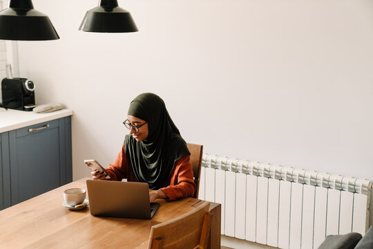 Young woman in hijab and glasses looking on her phone