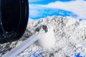 Closed up shot of a scoop of creatine powder next to a bottle.