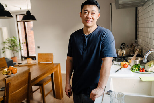Adult brunette asian man wearing t-shirt smiling in kitchen at home