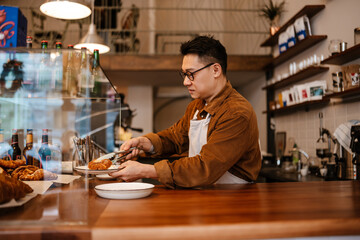 Adult asian man holding plate with croissant at counter in cafe