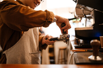 Adult asian man making coffee with machine while working in cafe