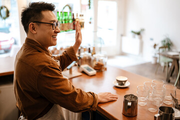Asian man standing at counter with cup of coffee while working in cafe