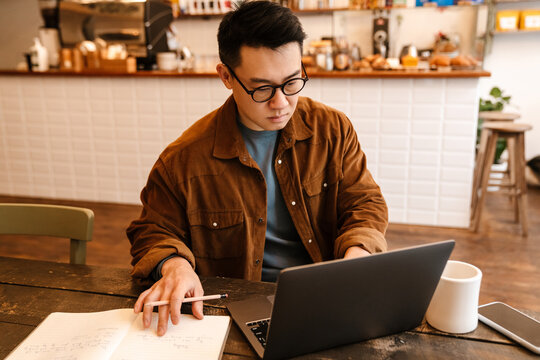 Adult asian man working with laptop and paper documents in cafe