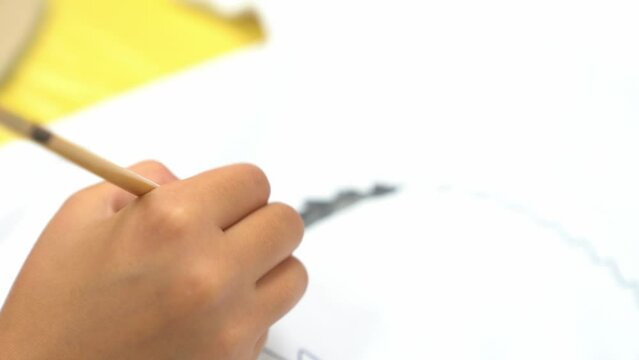 A little girl draws a hedgehog with gray acrylic paint on a fabric. Draws on a white T-shirt. The child's work on the fabric. The concept of child development. High quality 4k footage