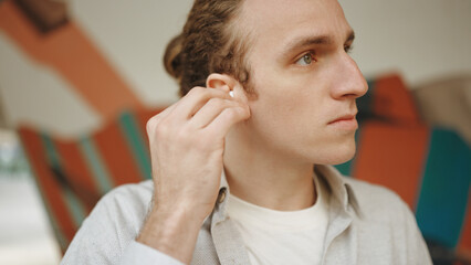 Young white curly man using earphones while standing outdoors