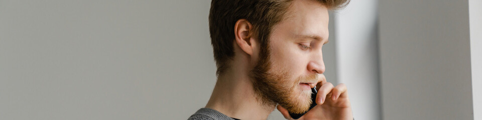 Obraz premium Ginger young man talking on mobile phone while standing indoors