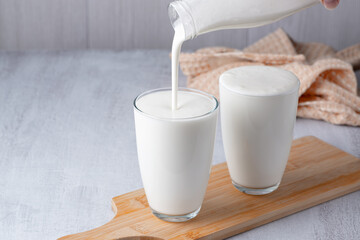 Pouring homemade kefir, buttermilk or yogurt with probiotics. Yogurt flowing from glass bottle on light background. Probiotic cold fermented dairy drink. Trendy food and drink. Copy space.