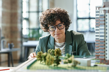 Young female designer in eyeglasses looking at her construction mock-up and thinking over new details