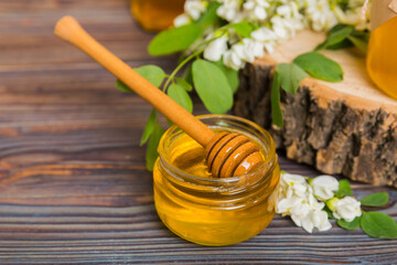 Sweet honey jar surrounded spring acacia blossoms. Honey flows from a spoon in a jar. jars of clear fresh acacia honey on wooden background