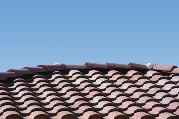 Close-up of a section of a red brown tile roof under blue sky
