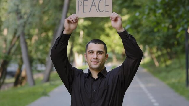 Strong patriotic man handsome smiling caucasian businessman guy raise up paper cardboard with lettering word peace hold painted placard against violence asking help for Ukraine peaceful artwork symbol