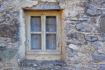 Fototapeta na wymiar Closeup of a wooden window in a stone wall of an old grey house. Boarded up square window frame in a historic rustic building. Architecture and background of a rural structure outside with copyspace