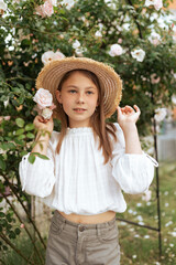 cute little girl with a straw hat for a bush of white roses