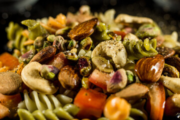 pasta salad, with nuts, tomato and condiments on black background