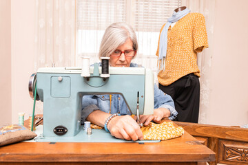 elderly woman sewing an orange cloth with an antique sewing machine