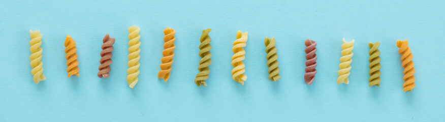 Heaps of pasta - various colors farfalle pasta on blue background, top view