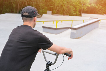 athletic young man on bmx bike in a cap stands in a concrete bmx skate park in sunlight