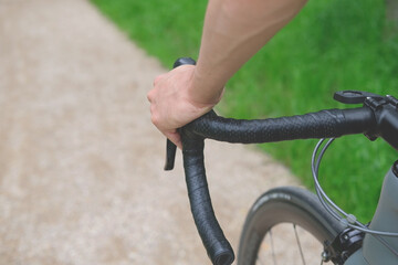 person holding a handlebar of cyclocross bike top grip close up, riding in a city park on gravel path