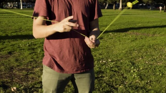 Young Man Wearing a Red T-Shirt Doing Cool Tricks on a Blue and Orange Counterweight Yoyo in a Field of Grass at Sunset with Palm Trees in the Background