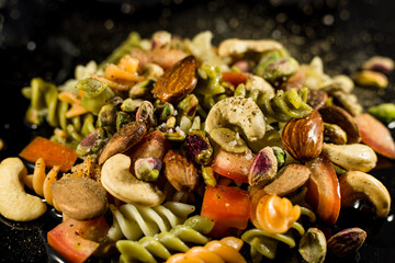 pasta salad, with nuts, tomato and condiments on black background