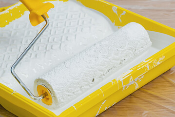 Paint roller in paint tray with white color. Repair and painting in the house. Construction and painting works.