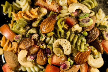 pasta salad, with nuts, tomato and condiments on black background