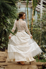Fototapeta premium A young girl in a vintage dress in a tropical greenhouse.