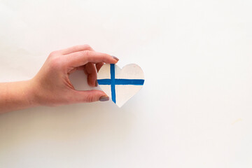 Paper heart in the colors of the flag of Finland in female hands.