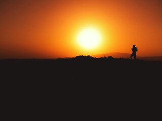 Fototapeta na wymiar Silhouette of a man with fedora hat on sunset on a hill