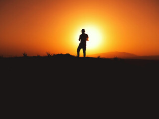 Silhouette of a man with fedora hat on sunset on a hill