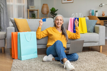 Cheerful european senior woman with gray hair uses credit card and laptop have success online...