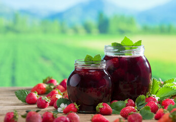 Strawberry jam jars on rustic table. Strawberry garden image in the background. Natural spring jams. Organic breakfast food concept.